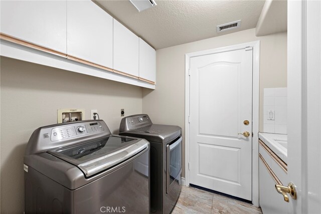 laundry area with washer and clothes dryer, cabinets, and a textured ceiling