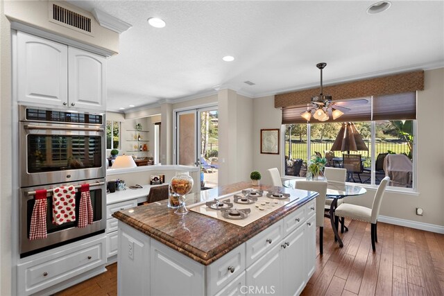 kitchen with white gas cooktop, white cabinets, a kitchen island, dark hardwood / wood-style flooring, and stainless steel double oven