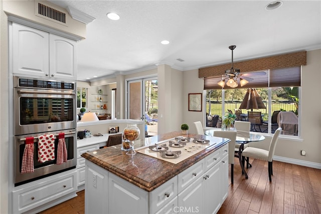 kitchen featuring stainless steel double oven, white gas stovetop, a kitchen island, visible vents, and crown molding