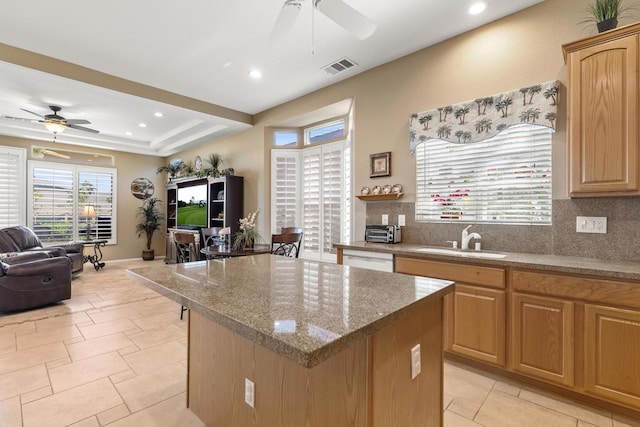 kitchen featuring sink, light tile patterned floors, a kitchen island, ceiling fan, and backsplash