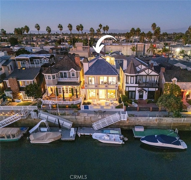 back house at dusk featuring a balcony and a water view