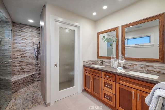 bathroom with tile patterned floors, vanity, a tile shower, and backsplash