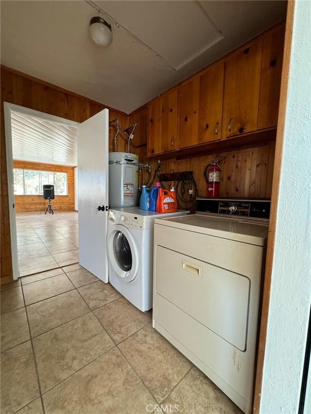 laundry area with strapped water heater, cabinets, wooden walls, light tile patterned flooring, and washer and dryer