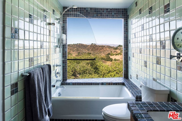 bathroom with a tub to relax in, tile walls, and toilet