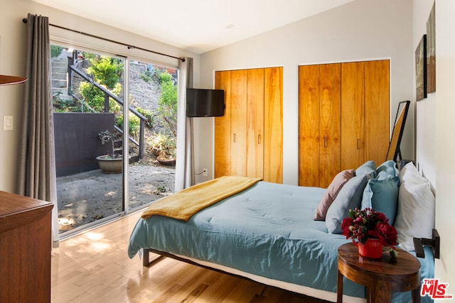 bedroom with access to exterior, hardwood / wood-style floors, two closets, and vaulted ceiling