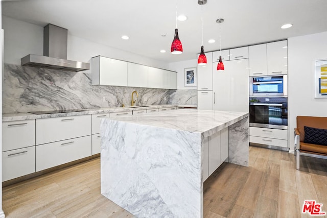 kitchen with a large island, wall chimney range hood, light hardwood / wood-style floors, black electric stovetop, and white cabinets