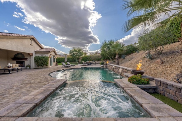 view of pool with pool water feature, an outdoor fireplace, and a patio