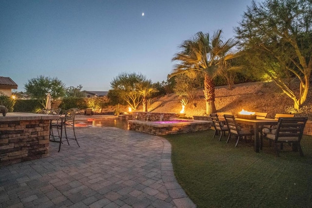 patio terrace at dusk featuring a swimming pool with hot tub and exterior bar