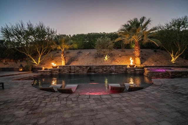 pool at dusk with an in ground hot tub and a patio