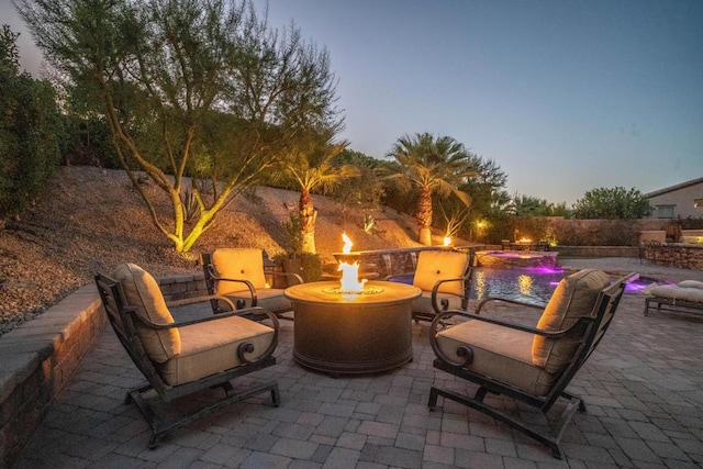 patio terrace at dusk with pool water feature, an outdoor fire pit, and a fenced in pool