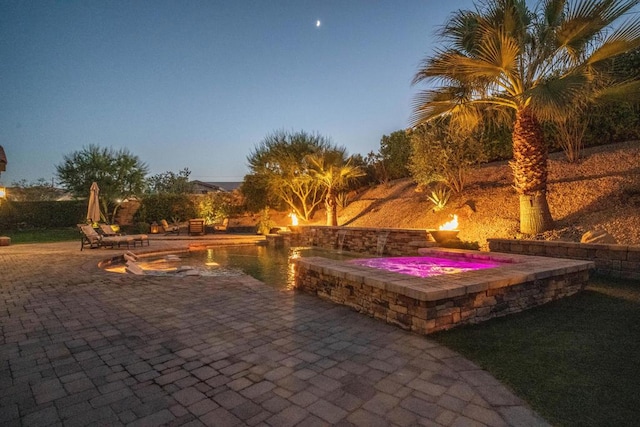 patio terrace at dusk featuring a pool with hot tub