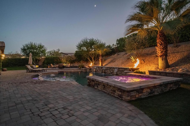 patio terrace at dusk featuring a pool with hot tub and pool water feature