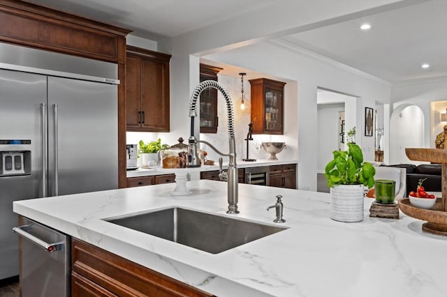 kitchen featuring light stone counters, sink, high quality fridge, and ornamental molding