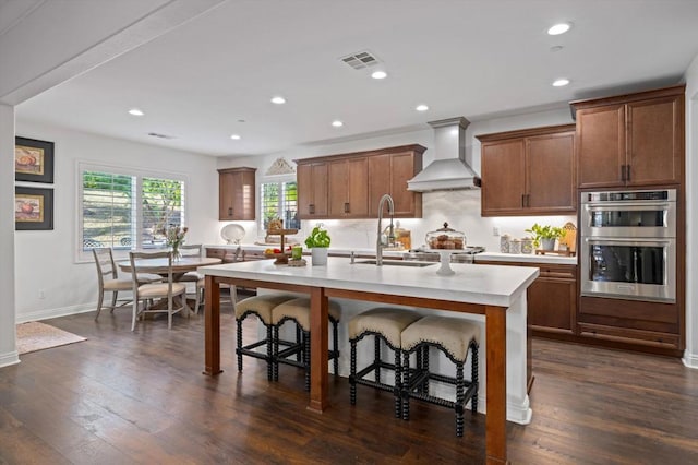 kitchen featuring custom exhaust hood, sink, appliances with stainless steel finishes, an island with sink, and a breakfast bar area