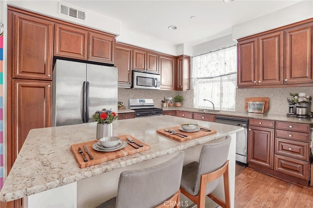 kitchen featuring light stone counters, appliances with stainless steel finishes, a kitchen bar, a kitchen island, and light wood-type flooring