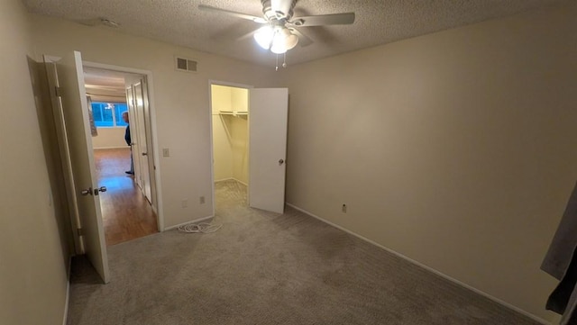 unfurnished bedroom featuring a textured ceiling, ceiling fan, a closet, a walk in closet, and light colored carpet