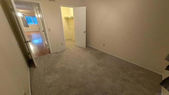 unfurnished bedroom with a spacious closet, a closet, and carpet floors