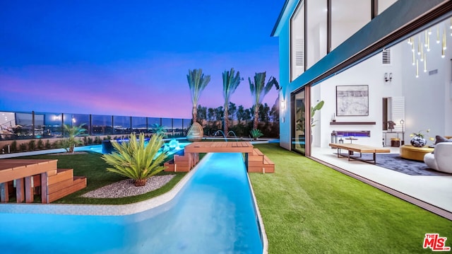 pool at dusk featuring pool water feature, a patio area, and a yard