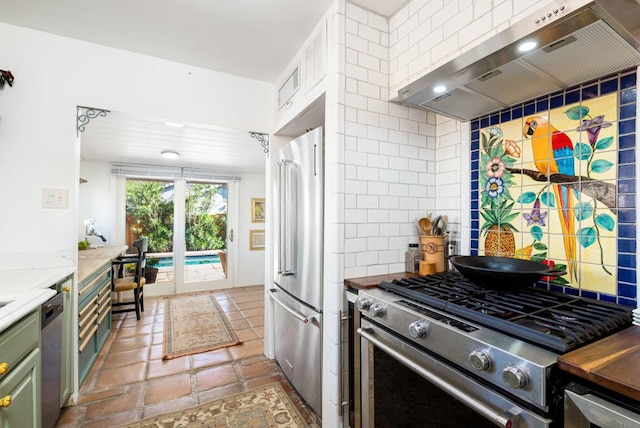 kitchen with light stone countertops, wall chimney exhaust hood, high quality appliances, and decorative backsplash