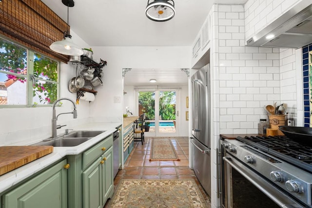 kitchen with tasteful backsplash, wall chimney exhaust hood, premium appliances, sink, and green cabinetry