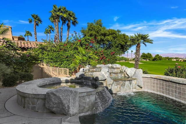 view of swimming pool with pool water feature and a hot tub