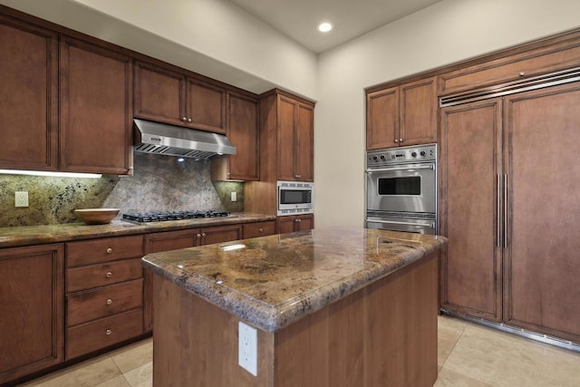 kitchen with built in appliances, decorative backsplash, a center island, and dark stone counters