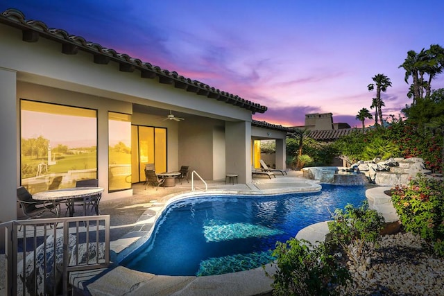 pool at dusk featuring ceiling fan, an in ground hot tub, and a patio