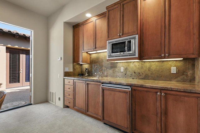 kitchen with stainless steel microwave, light carpet, dark stone counters, sink, and decorative backsplash