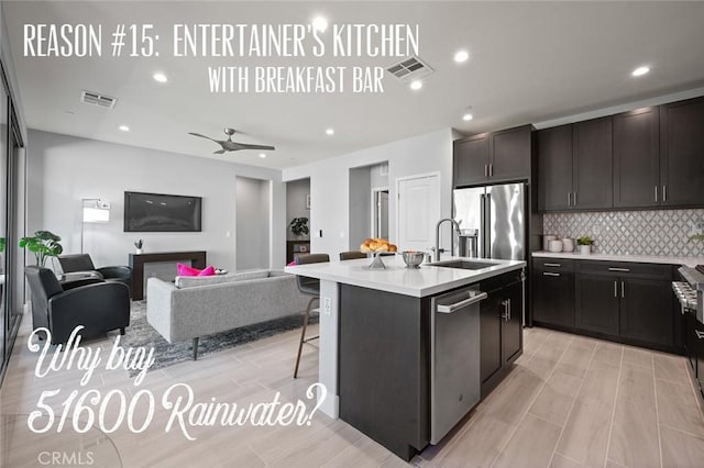 kitchen featuring ceiling fan, stainless steel appliances, an island with sink, decorative backsplash, and a breakfast bar