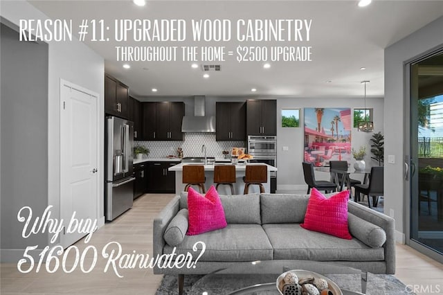 kitchen with backsplash, wall chimney exhaust hood, an island with sink, light hardwood / wood-style floors, and stainless steel appliances