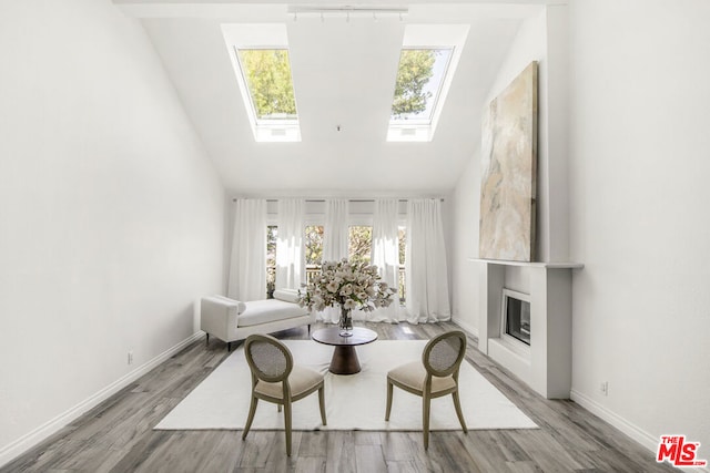 living area featuring light wood-type flooring, high vaulted ceiling, and a skylight