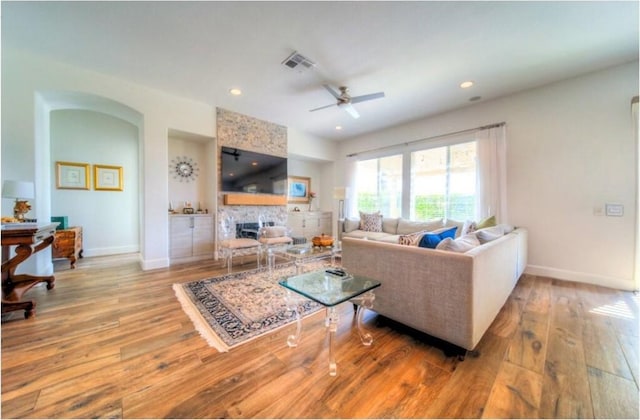 living room with a fireplace, light wood-type flooring, and ceiling fan