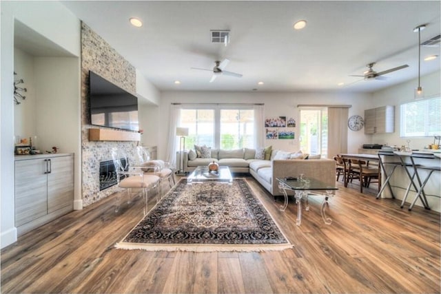 living room with hardwood / wood-style floors, ceiling fan, and a stone fireplace