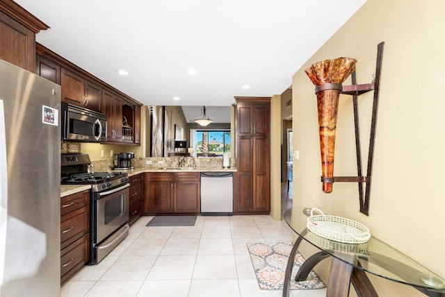 kitchen featuring light stone countertops, appliances with stainless steel finishes, sink, light tile patterned floors, and decorative light fixtures