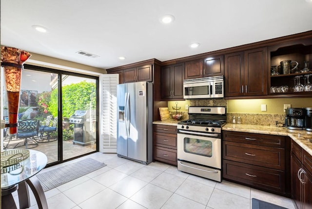 kitchen featuring decorative backsplash, light tile patterned floors, light stone counters, dark brown cabinetry, and stainless steel appliances