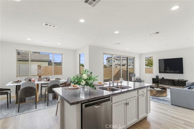 kitchen with sink, dishwasher, an island with sink, dark stone counters, and white cabinets