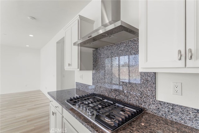 kitchen featuring wall chimney range hood, white cabinetry, tasteful backsplash, stainless steel gas cooktop, and dark stone counters