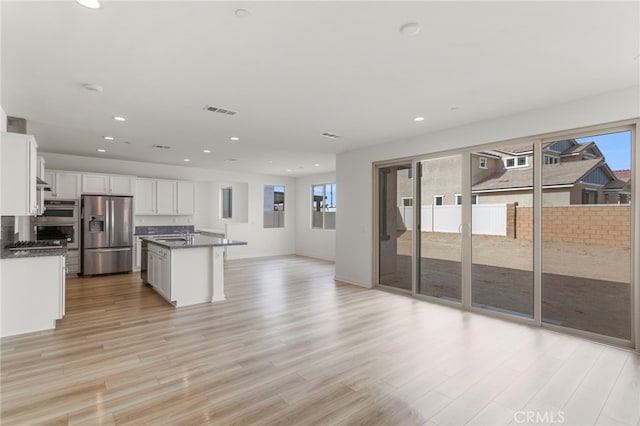 kitchen with white cabinetry, stainless steel refrigerator with ice dispenser, an island with sink, and light hardwood / wood-style floors