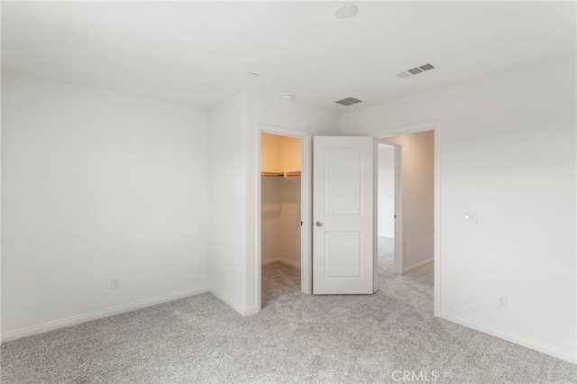 unfurnished bedroom featuring a spacious closet, light carpet, and a closet