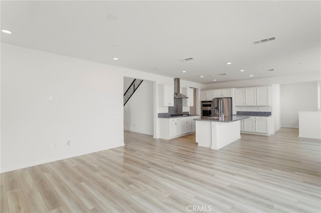 kitchen with white cabinets, appliances with stainless steel finishes, wall chimney exhaust hood, and a center island with sink