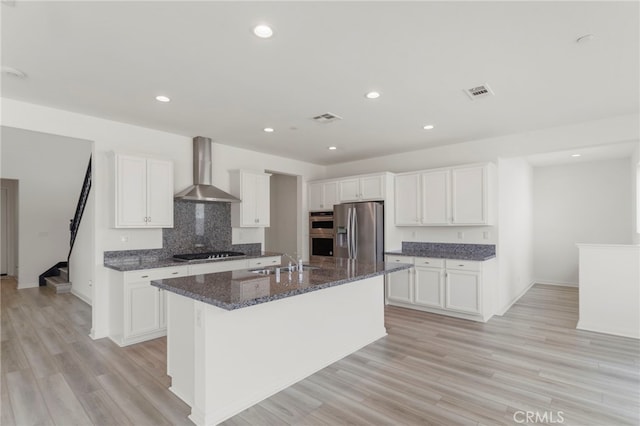 kitchen with appliances with stainless steel finishes, a center island with sink, white cabinets, and wall chimney exhaust hood