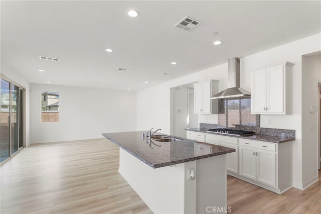 kitchen with sink, white cabinetry, an island with sink, stainless steel gas cooktop, and wall chimney exhaust hood