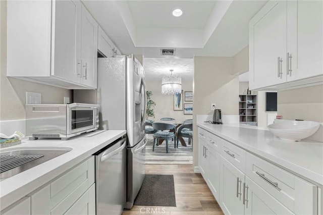 kitchen with light hardwood / wood-style flooring, an inviting chandelier, a tray ceiling, white cabinets, and stainless steel dishwasher