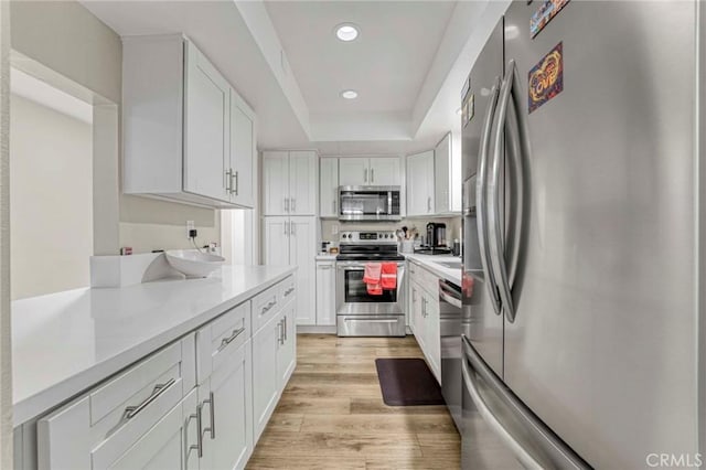 kitchen featuring a raised ceiling, white cabinetry, appliances with stainless steel finishes, and light hardwood / wood-style flooring