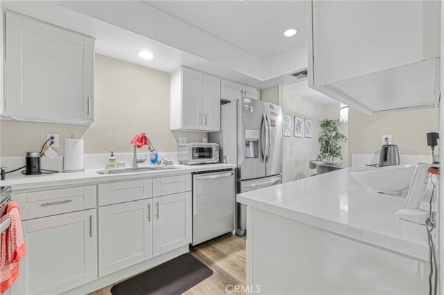 kitchen featuring white cabinetry, stainless steel appliances, sink, and light wood-type flooring