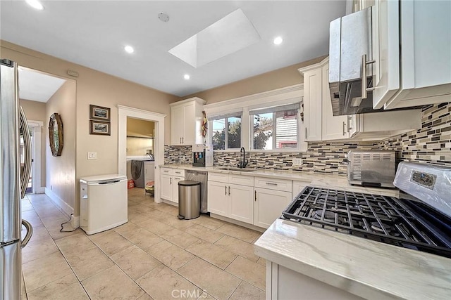 kitchen featuring a skylight, decorative backsplash, appliances with stainless steel finishes, white cabinetry, and washer / clothes dryer