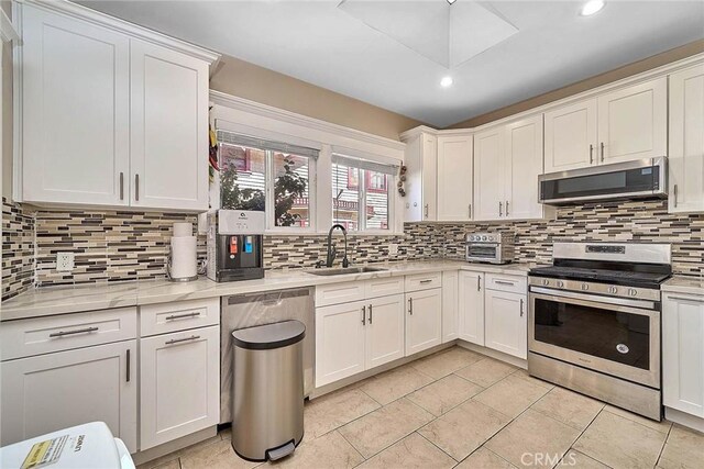 kitchen featuring sink, stainless steel appliances, light stone counters, decorative backsplash, and white cabinets