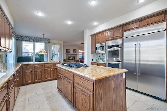 kitchen featuring a kitchen island, built in appliances, light tile patterned floors, and decorative light fixtures