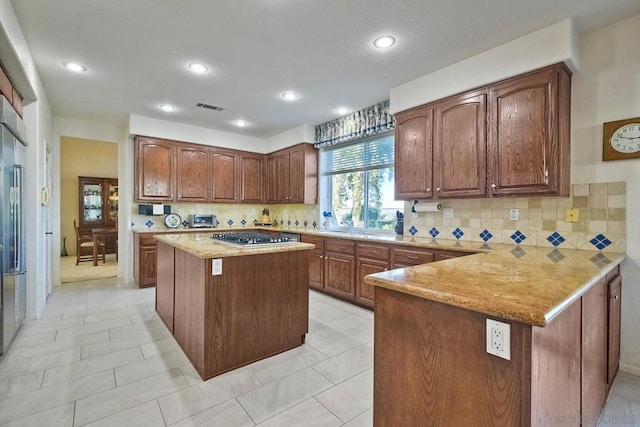 kitchen with decorative backsplash, kitchen peninsula, stainless steel gas stovetop, and a kitchen island