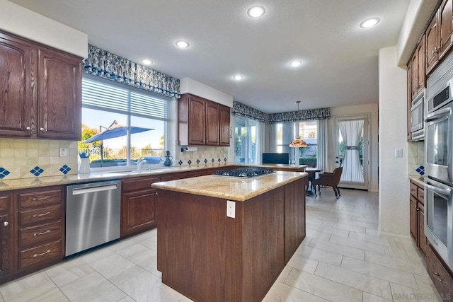 kitchen featuring sink, appliances with stainless steel finishes, tasteful backsplash, a kitchen island, and decorative light fixtures